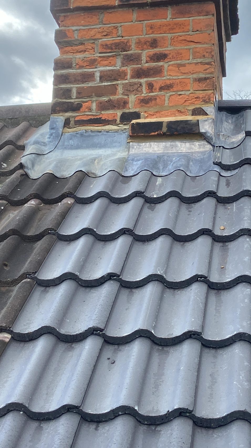 Fresh lead flashing dressed around a red brick chimney where it meets the new tiles