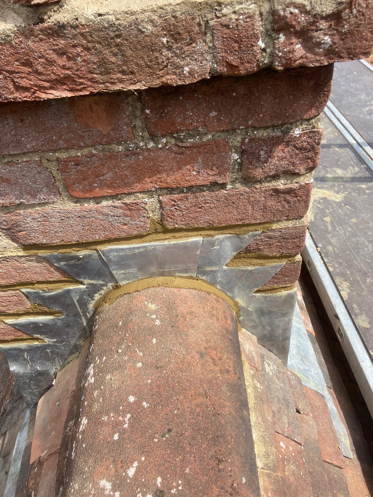 Re-bedded ridge line on a tiled roof beside a repointed chimney