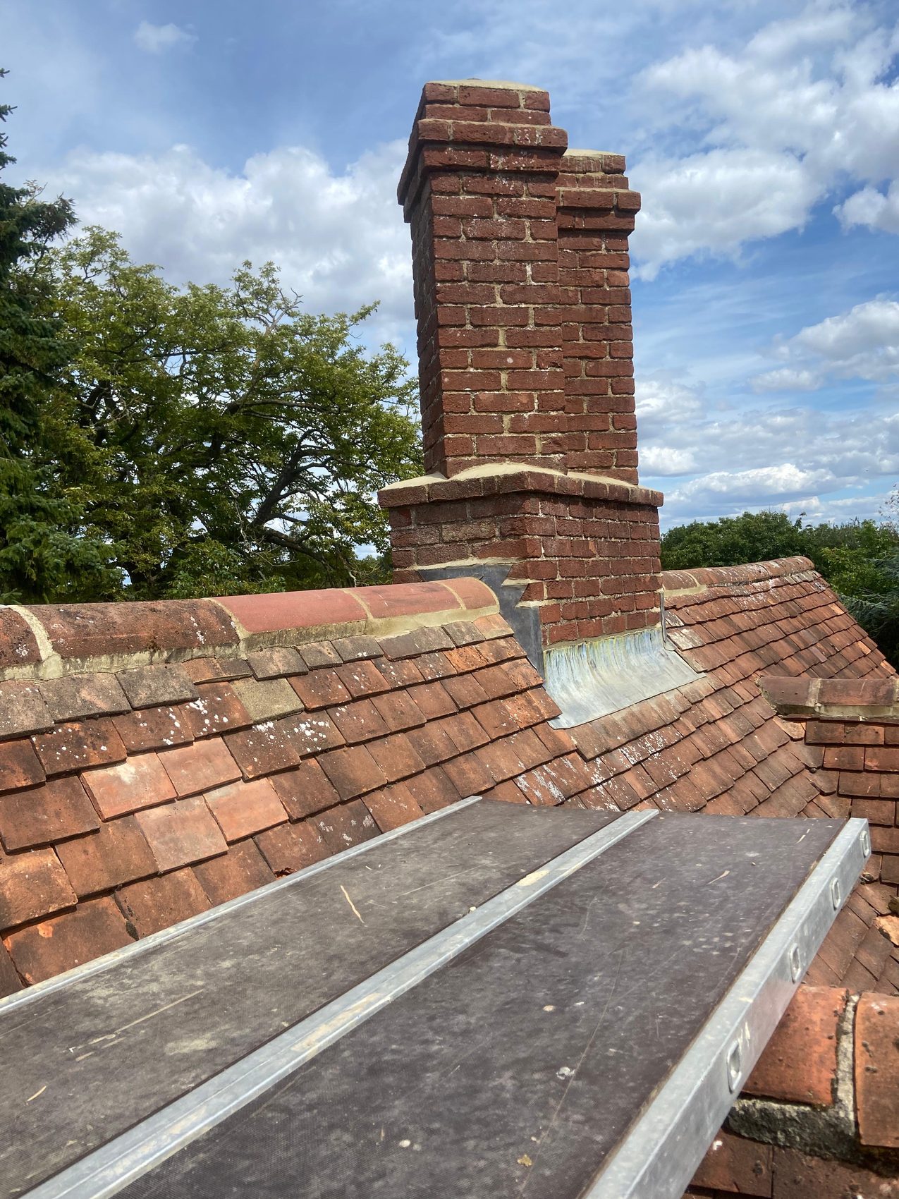 Repointed brick chimney stack with fresh lead flashing against a blue sky