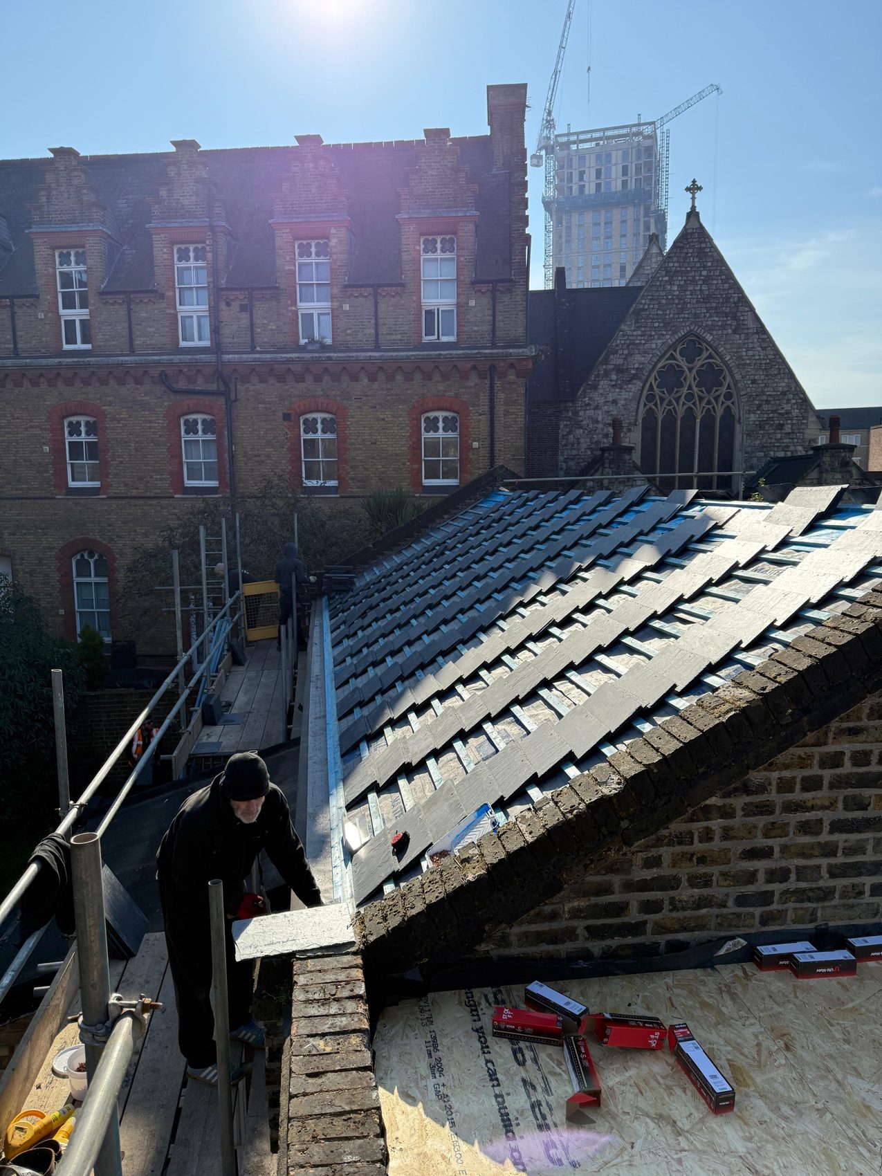 Natural slate being laid on a North London roof, with the heritage Gothic church and its cross standing behind