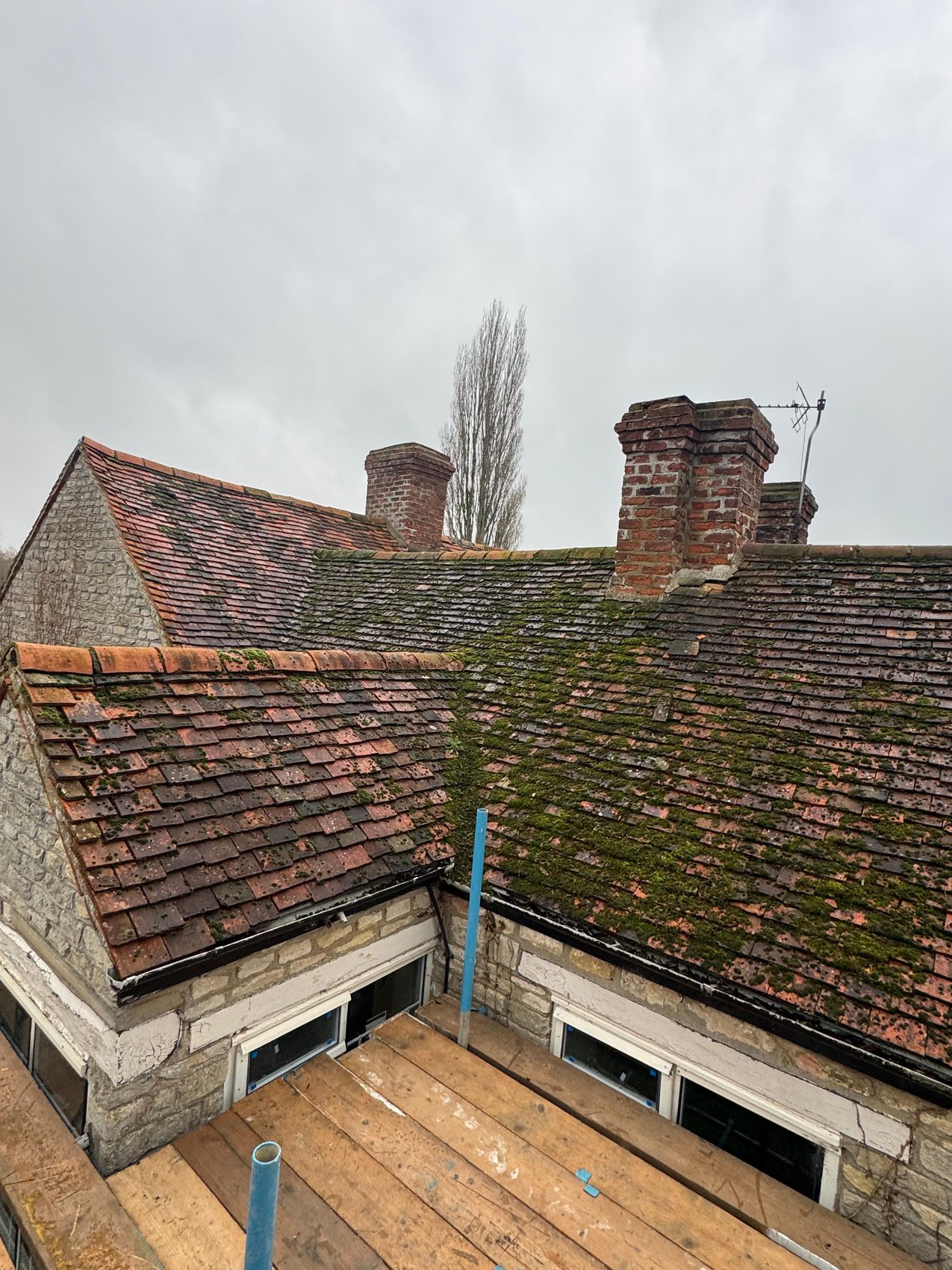 Original brick chimney stacks rising above the moss-covered mill roof