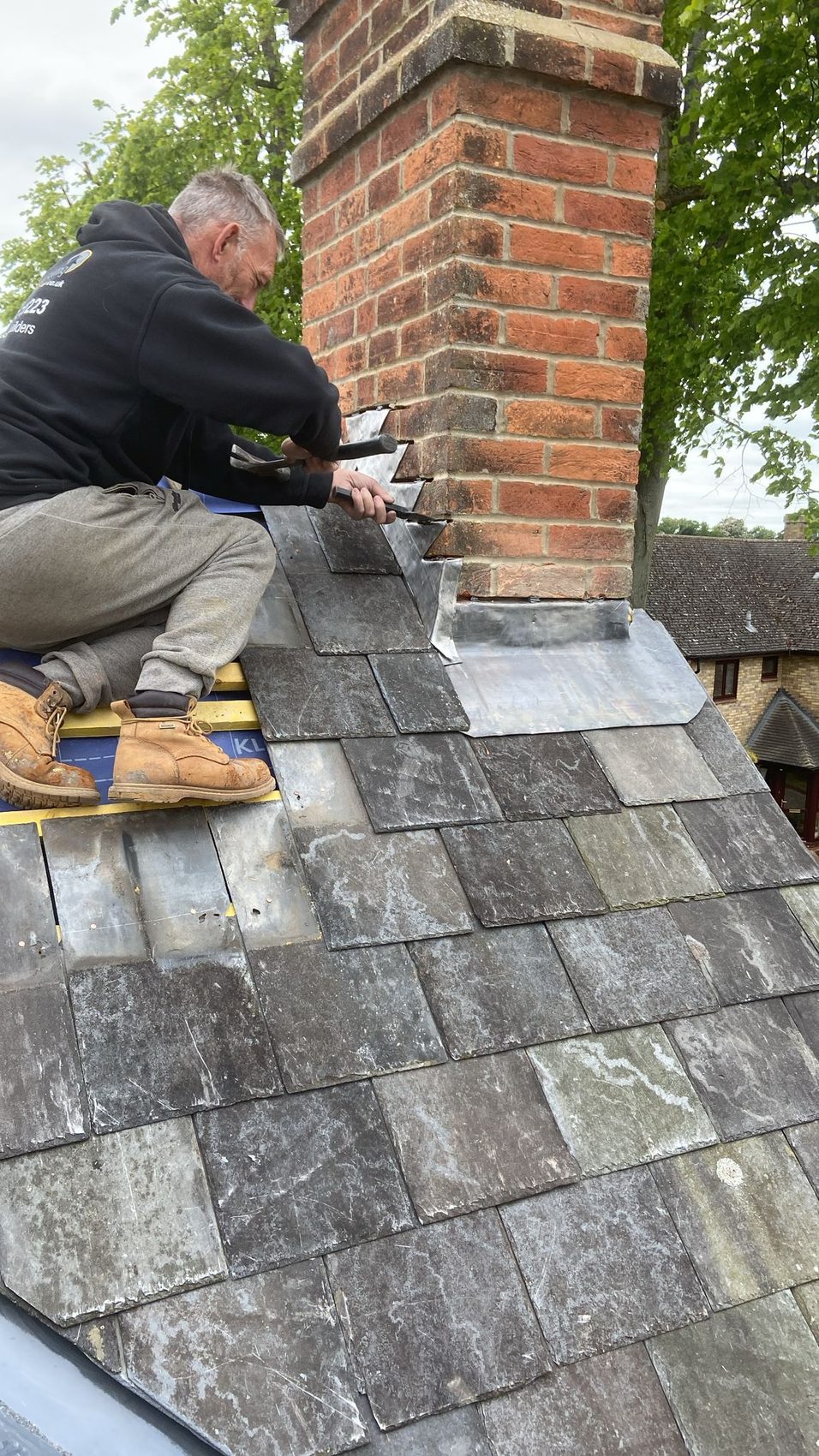 Roofer dressing lead soakers and weatherings around the brick chimney